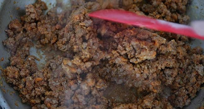 mixing tomato paste with cooked ground lamb and mirepoix