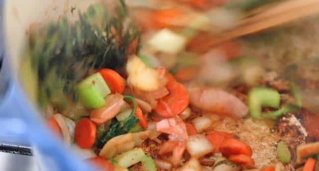 cooking mirepoix and herbs in a pot