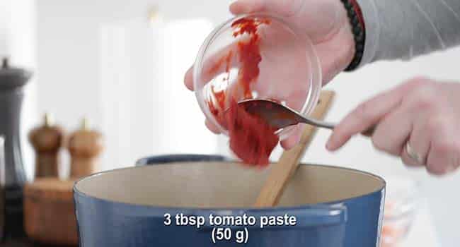 adding tomato paste to a pot