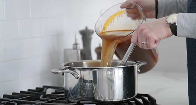 adding strained shrimp stock to a pot with roux