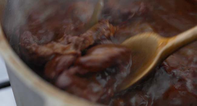 adding seared beef to a pot with braising liquid