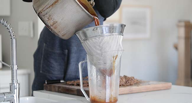 straining birria consome through a chinois