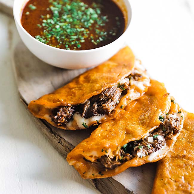 birria tacos on a cutting board next to a bowl of birria consome