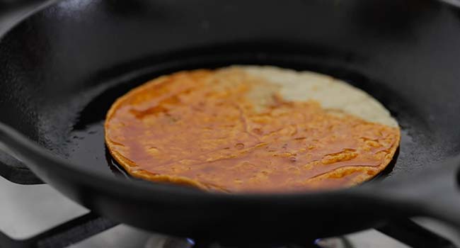 corn tortilla dipped in birria consome and fried in a pan