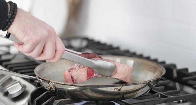 adding seasoned steak to a hot pan