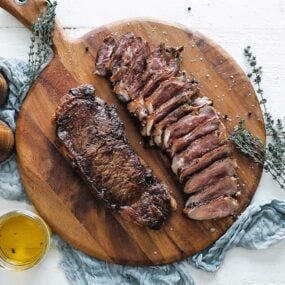 cutting board of seared steak and sliced steak