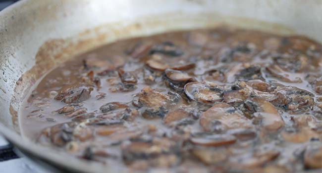 cooking beef stock with mushrooms in a pan to make a sauce