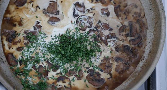 adding cream and parsley to a mushroom sauce