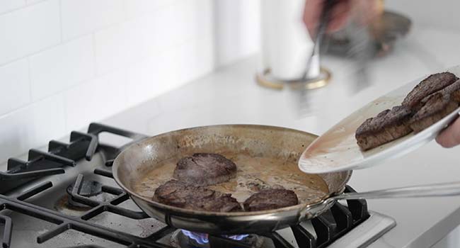 adding cooked filet mignon to a pan with mushroom sauce