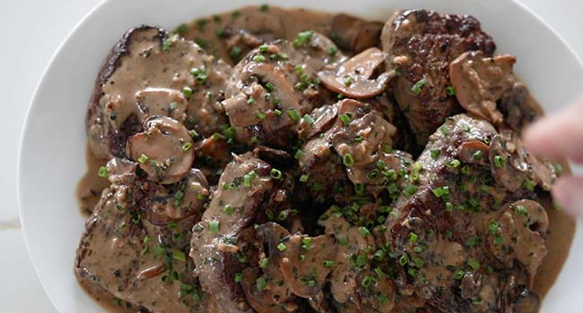 garnishing a platter of steak diane with sliced chives