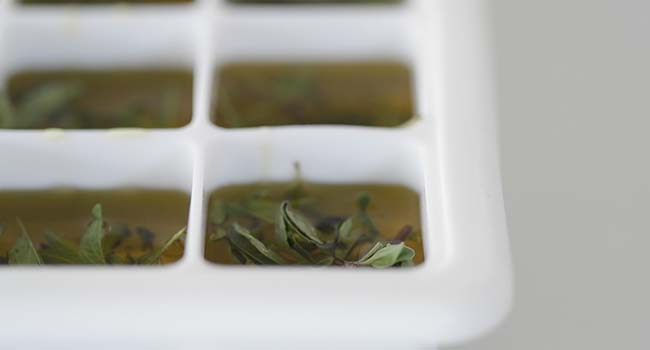 adding olive oil to a tray of fresh herbs