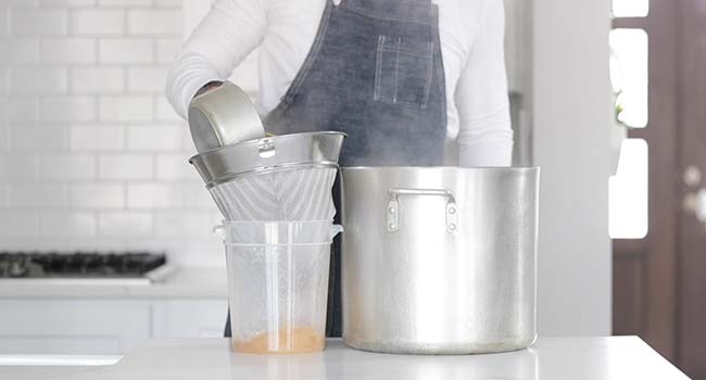 straining a homemade veggie stock through a chinois into a plastic container