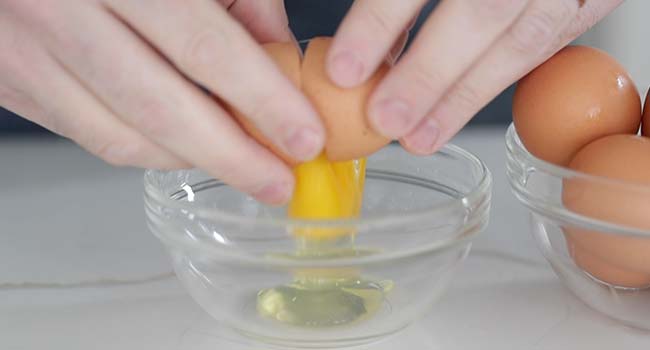 cracking an egg into a glass bowl