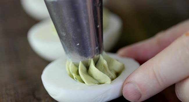 piping avocado deviled egg filling into hard boiled eggs