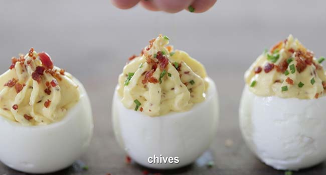 garnishing a deviled egg with bacon and chives
