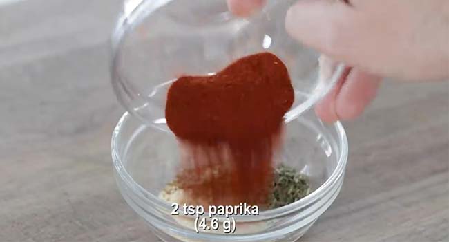 adding paprika to a bowl of seasoning