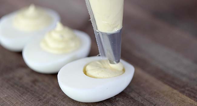 piping deviled egg filling into hard boiled egg halves