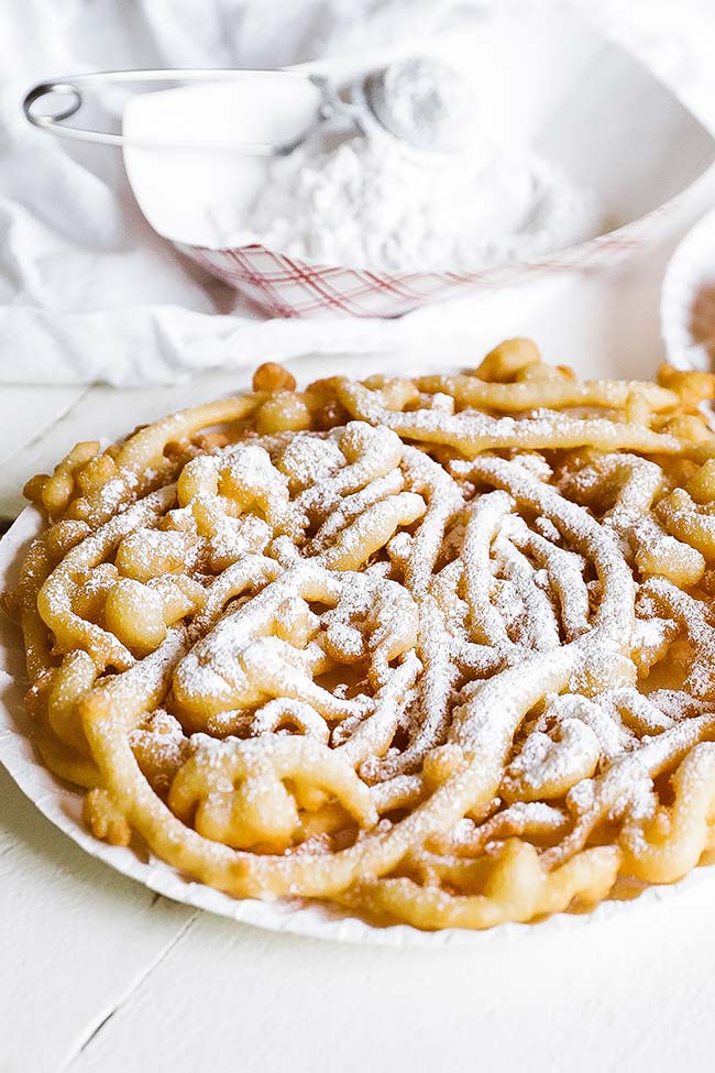 a fried funnel cake on a paper plate