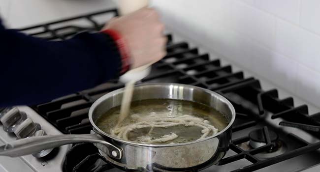 squeezing batter into hot oil in a pot