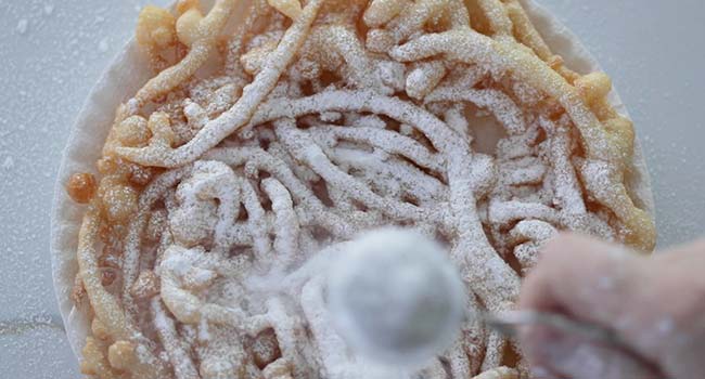 adding powdered sugar to a funnel cake