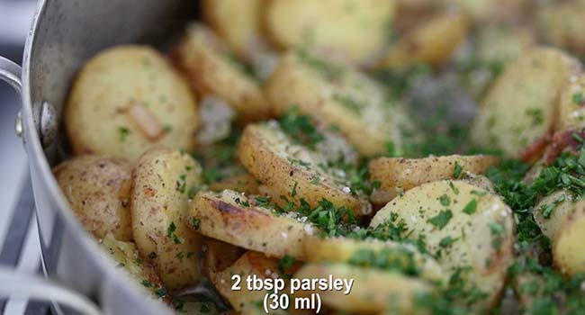 adding parsley to a pan of cooked potatoes