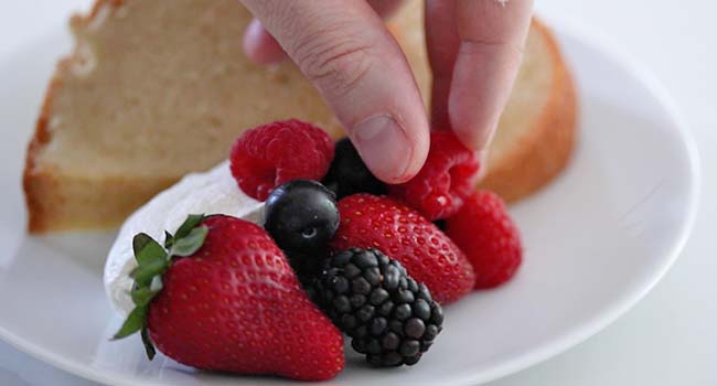 adding berries to a plate with pound cake