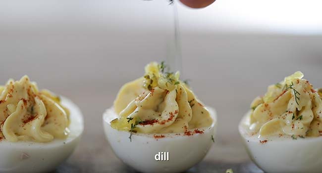 garnishing a southern deviled egg with sweet pickles and dill