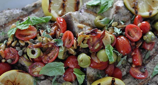 adding fresh herbs to a Sicilian swordfish