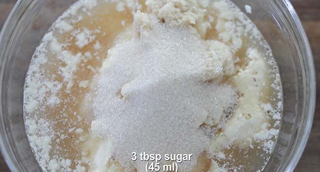 adding sugar to a bowl of white bbq sauce