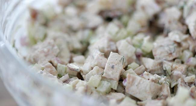 mixing together a chicken salad in a bowl