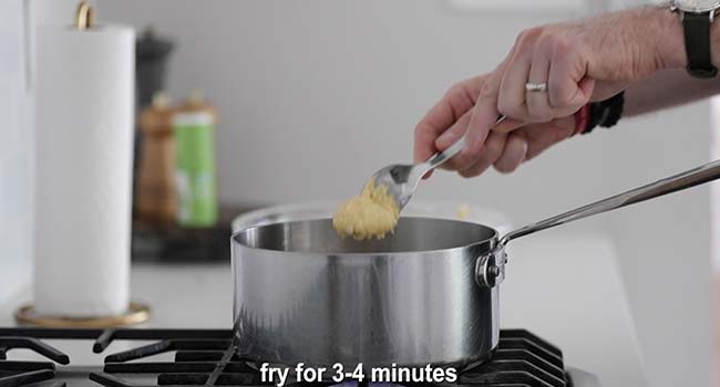 adding hush puppy batter to a pot of hot oil