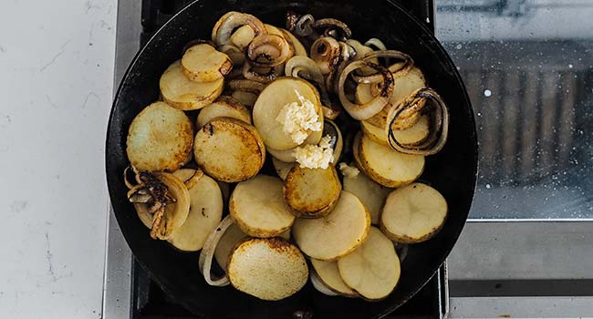 adding garlic to a pan of lyonnaise potatoes