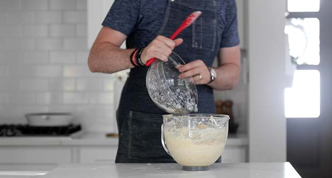 pouring blueberries into a bowl with blueberry muffin batter