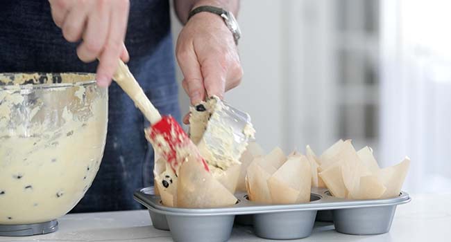 adding blueberry muffin batter to a a muffin tin