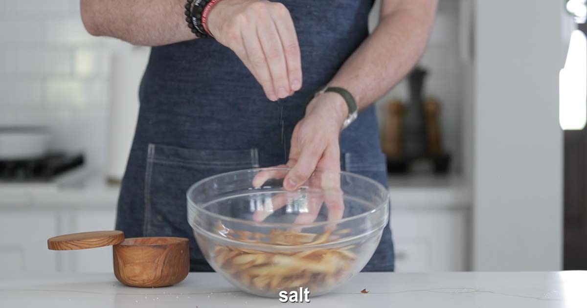 seasoning pommes frites with salt in a bowl