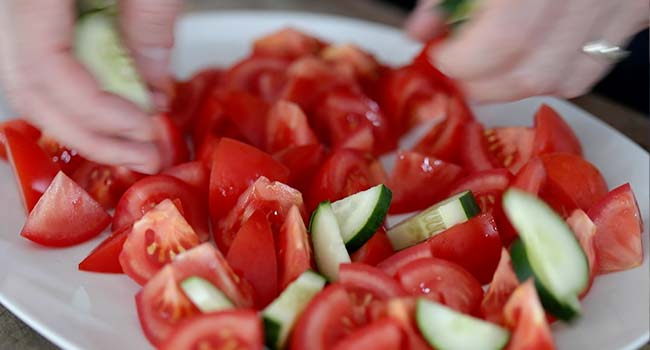 adding tomatoes and cucumbers to a platter