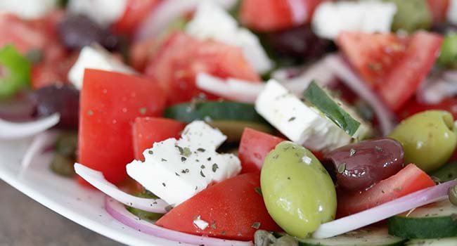 sprinkling herbs and olive oil on a Greek salad