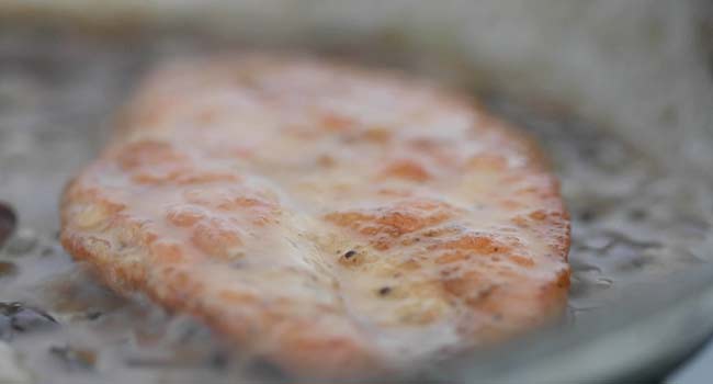 heating up a cooked chicken breast in a pan of mushroom gravy