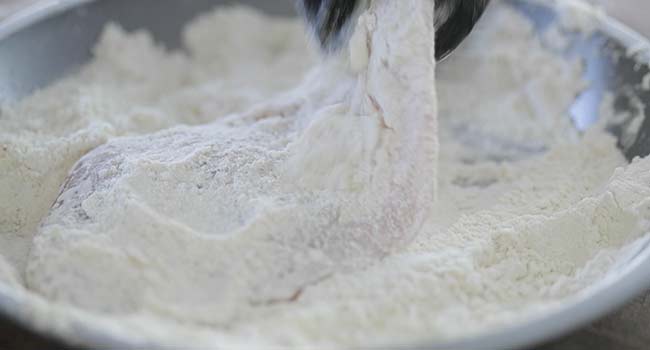 dredging chicken in a pan of seasoned flour