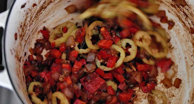 stirring garlic and peppers into a pot of onions