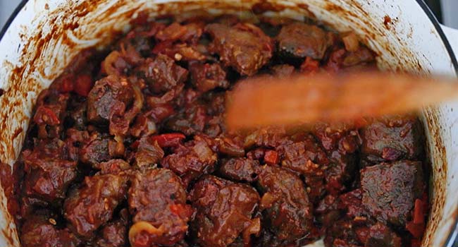 mixing cooked beef chunks with vegetables in a pot