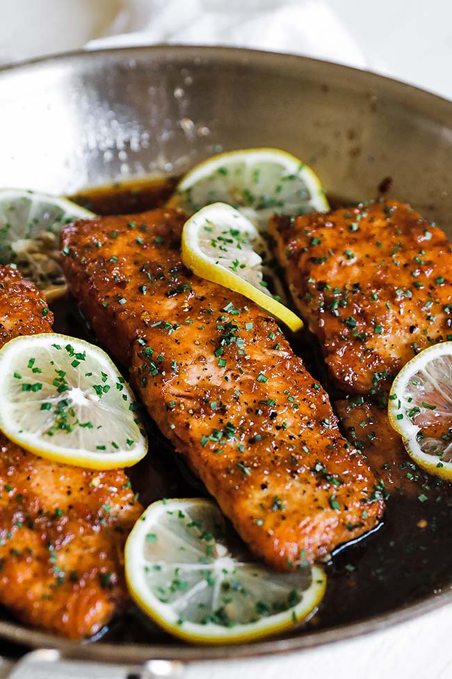 honey and garlic salmon fillets in a pan with lemon wheels
