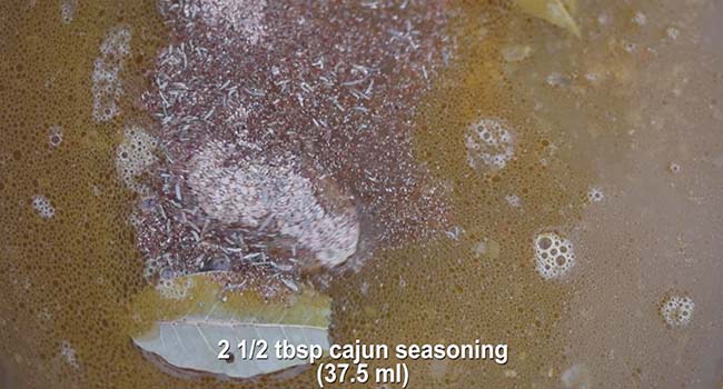 adding cajun seasoning to a pot of red beans