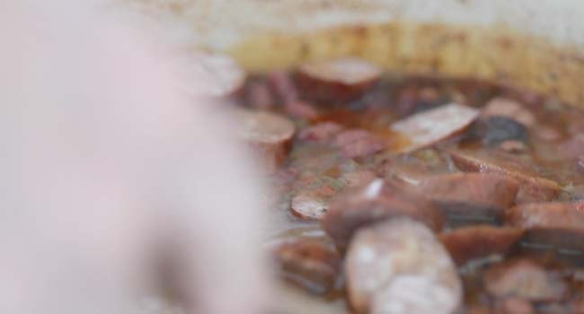 mixing sliced andouille sausage into a pot of red beans