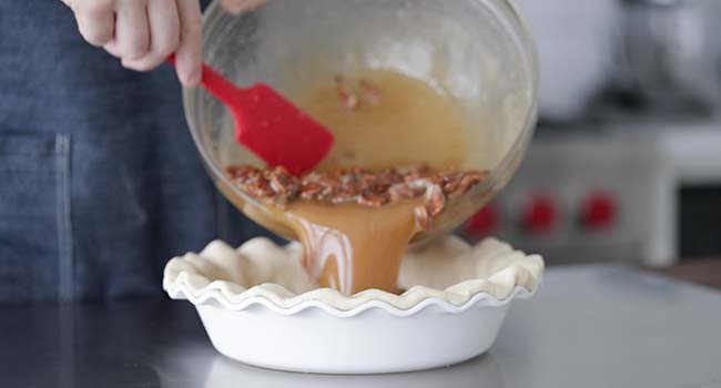 pouring pecan pie filling into a pie crust