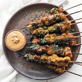 chicken satay skewers on a plate with peanut sauce