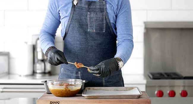 adding marinated chicken to skewers