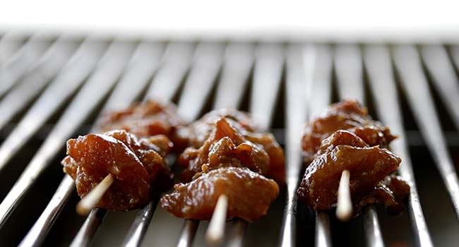 grilling chicken satay on a grill