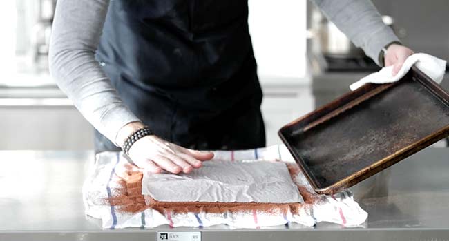 inverting a chocolate cake onto a cocoa dusted towel