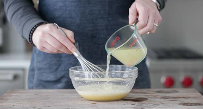 whisking hot chicken stock into eggs in a bowl